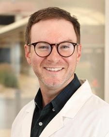 Dr. Sean Johnson headshot. Man with short heair and short beard wearing glasses and a lab coat.