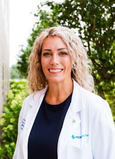 Dr. Tenkman, female appearance in a white lab coat with long curly hair.