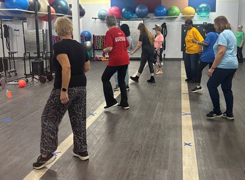 Dance fitness class at St. Joes At The Mall. Image of about a dozen people dressed in fitness clothes arranged in lines in dance studio.