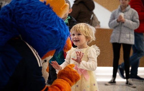 Young girl, about four years old, interacting with the FC Cincinnati lion mascot.